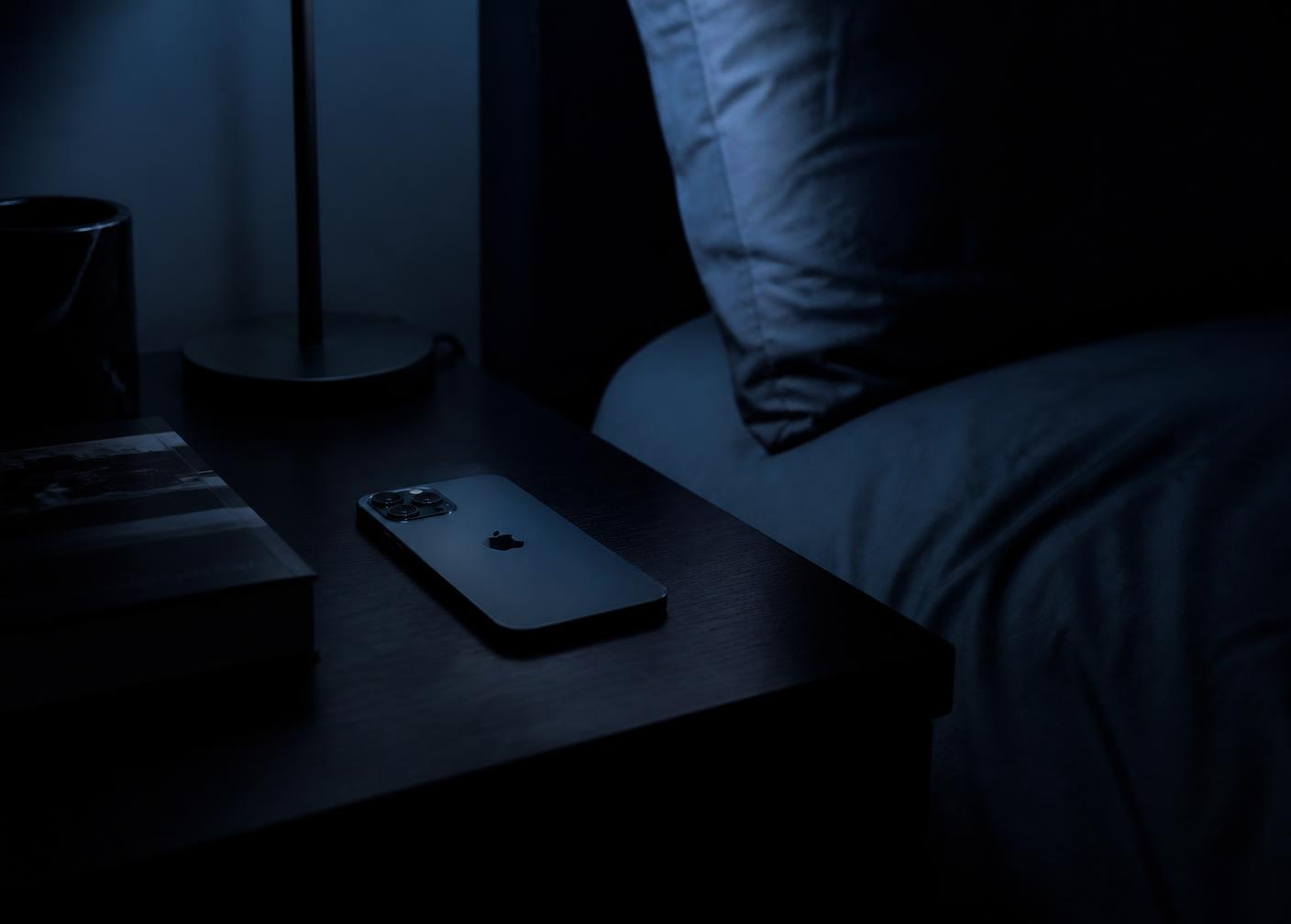 A phone resting on a nightstand beside a bed at night